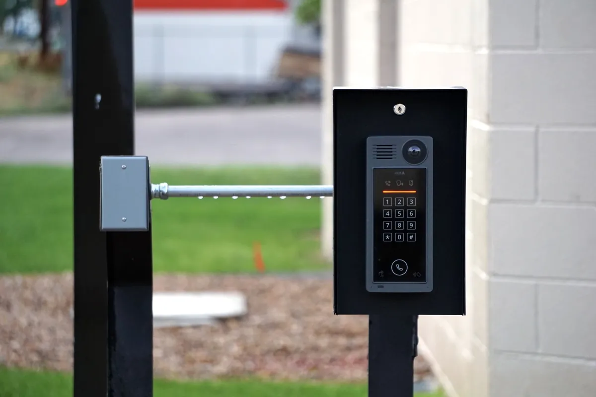 A keypad and intercom unit mounted at the entrance of a gated residential property, beside a barrier arm