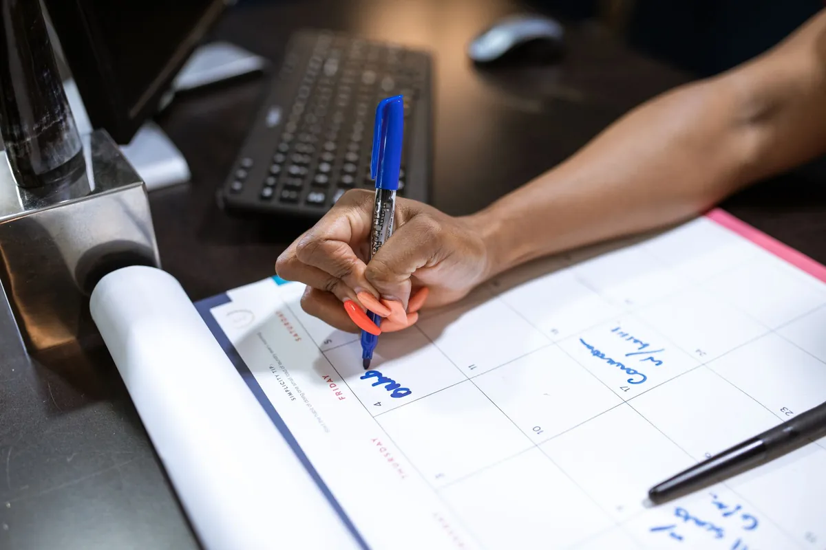 Two people drawing a weekly grid on a large sheet of paper at a desk