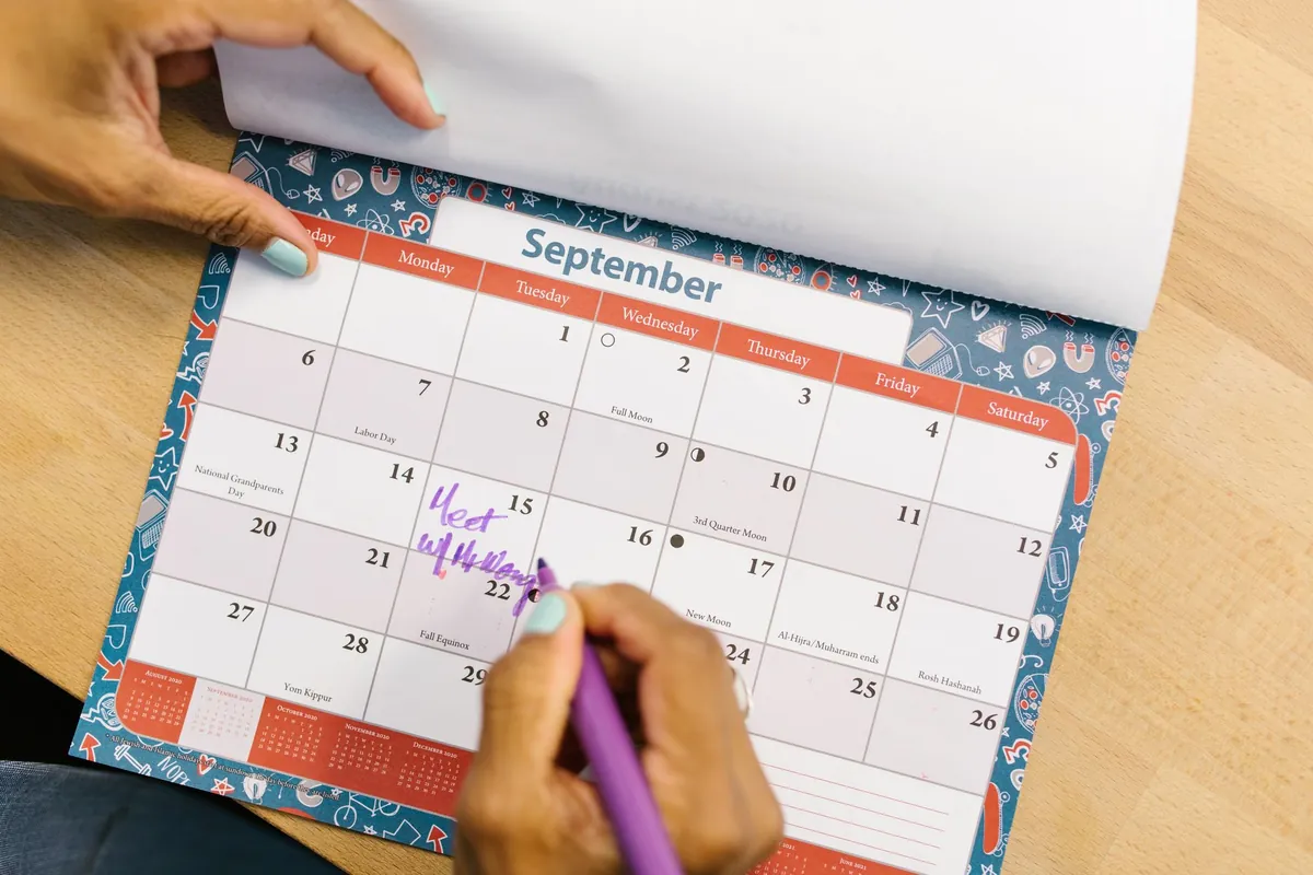 Hands marking a wall calendar with a purple pen