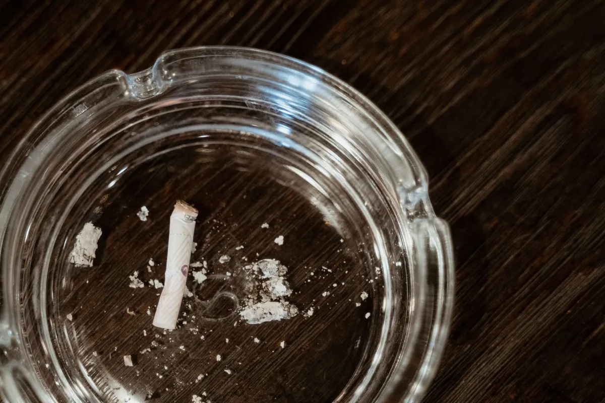 A single cigarette butt and ash in a glass ashtray, seen from above