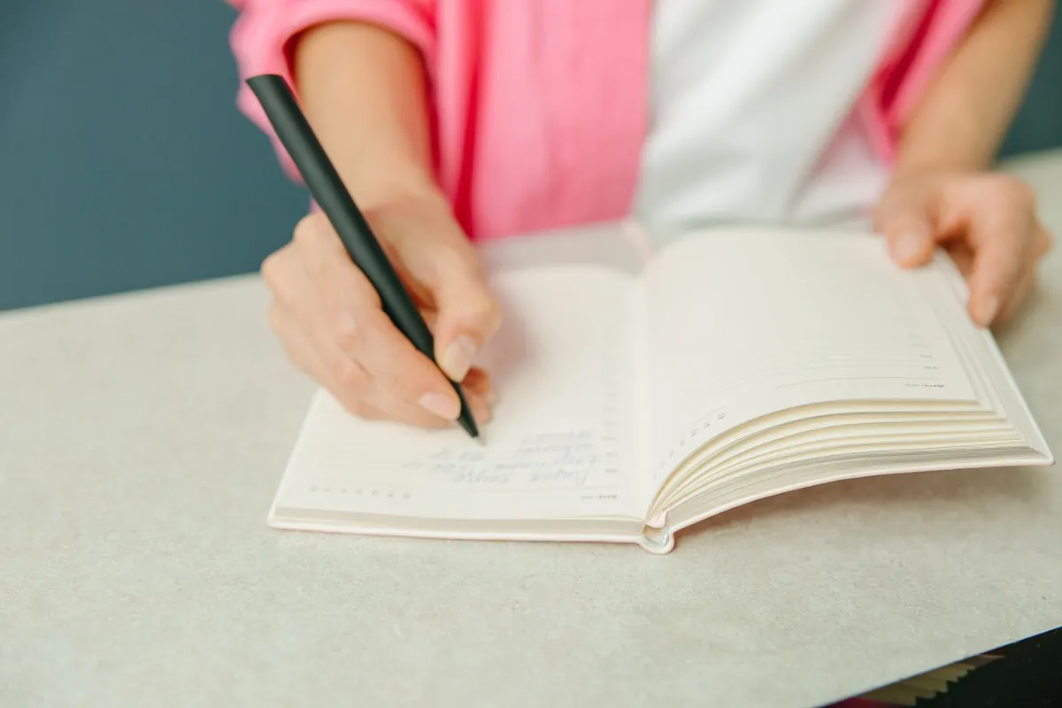 A close-up of a hand writing in a planner on a desk