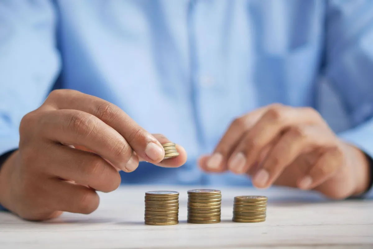 A hand adding a coin to three short stacks on a table