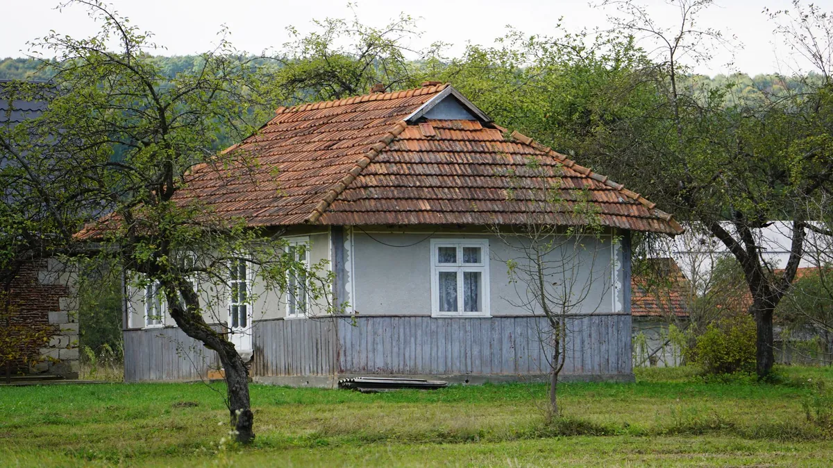 A rustic cottage with a tiled roof surrounded by trees