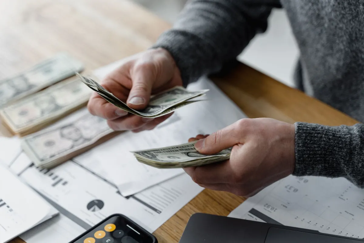 Hands counting banknotes over paperwork on a wooden table
