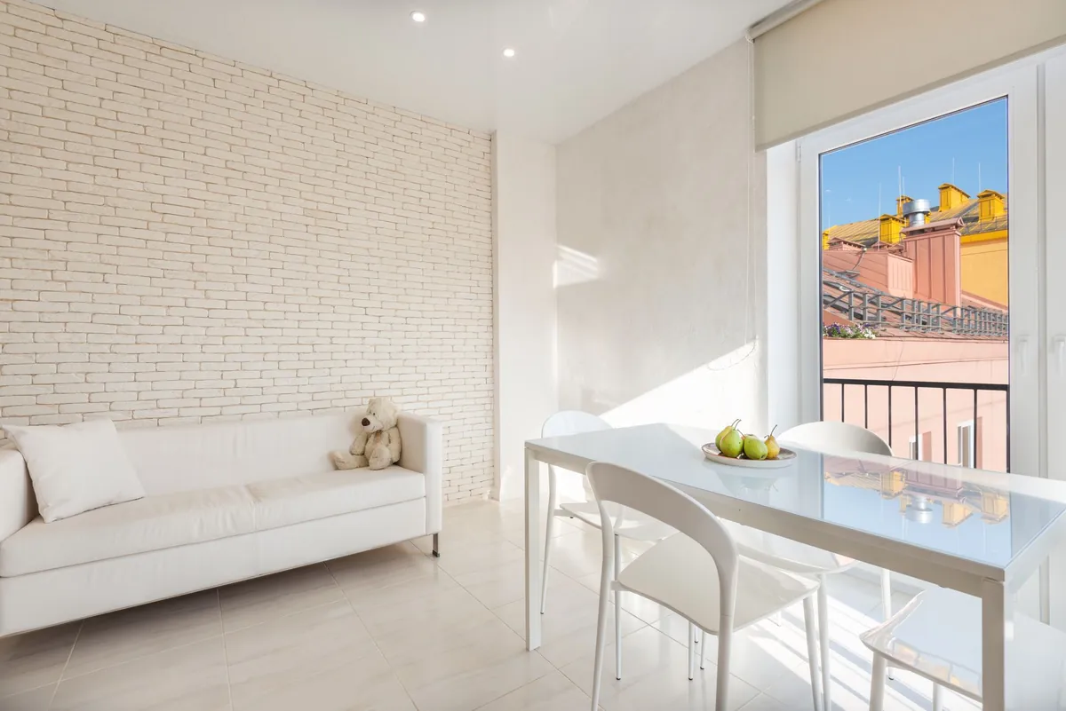 A minimal, sunlit room with a white sofa and a dining table by the window