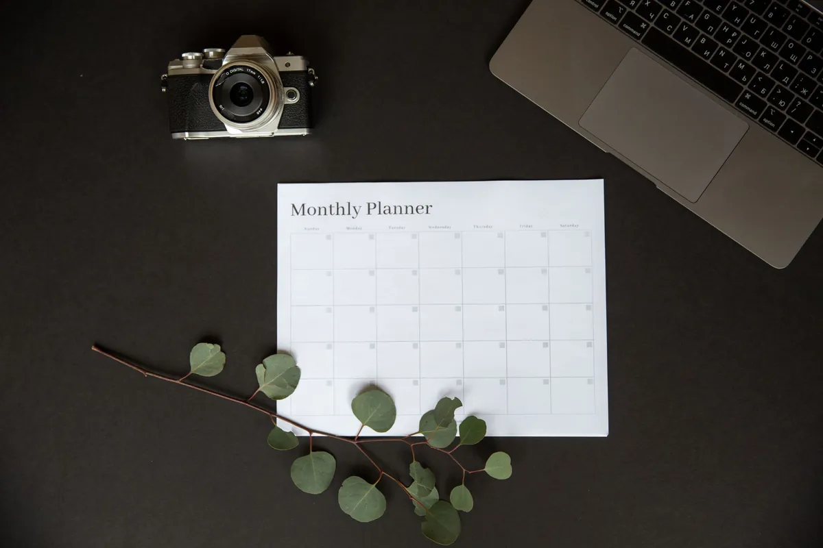 A blank monthly planner on a desk beside a laptop, used to map out which nights are already taken on each platform