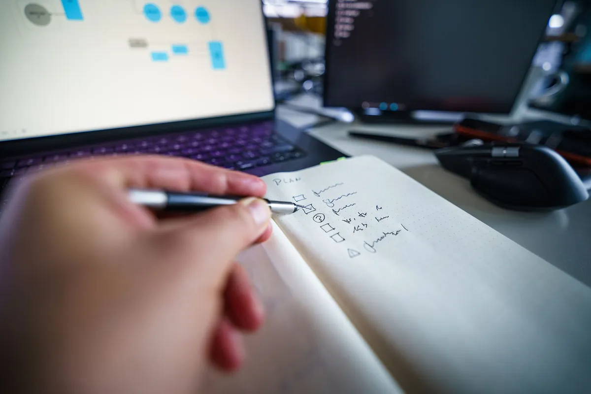 A host writing a short checklist in a notebook next to an open laptop while working through a calendar problem
