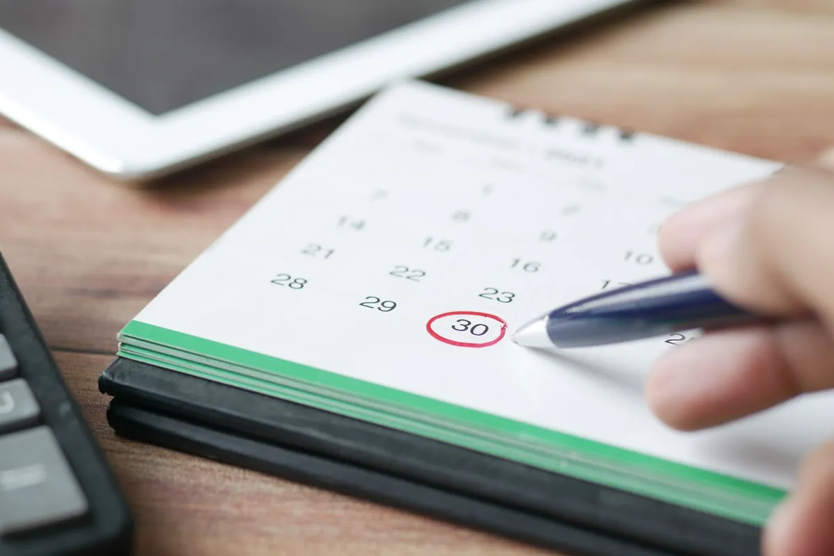 A hand circling a date on a desk calendar with a blue pen