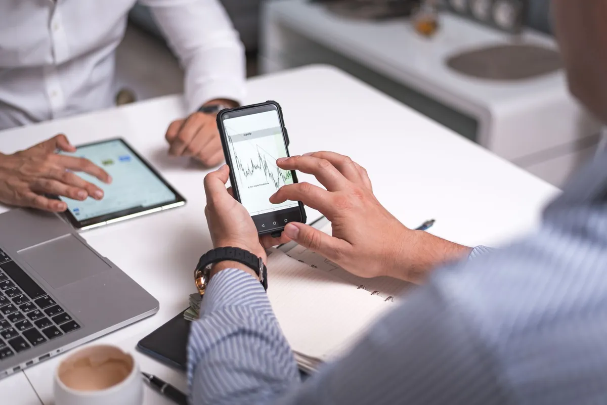 Two people comparing a phone and a tablet across a table