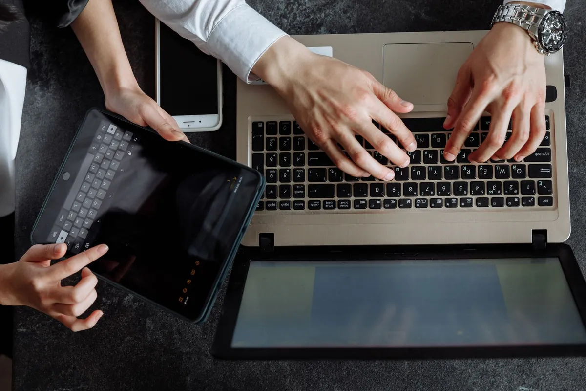 Two people working over a laptop and a tablet on a desk, seen from above