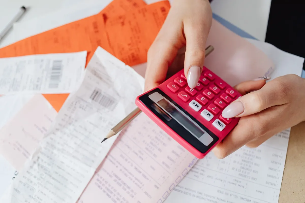 Hands working a calculator over a pile of paper receipts