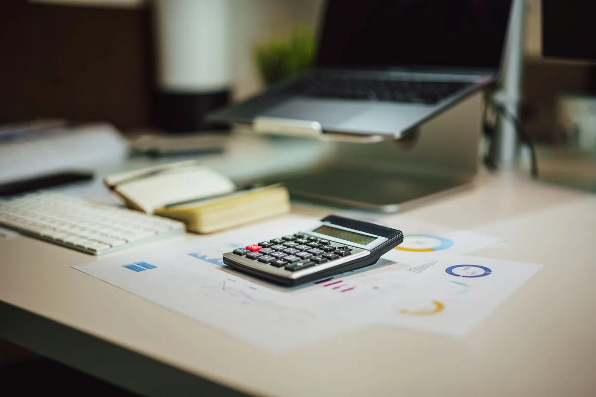 A calculator lying on printed charts on a desk next to a keyboard