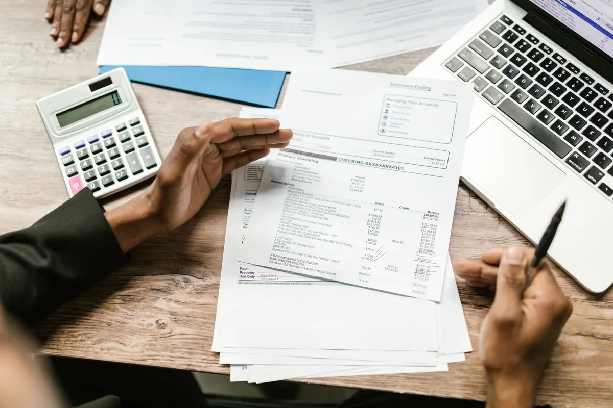 Hands with a calculator, printed statements and a laptop on a wooden desk