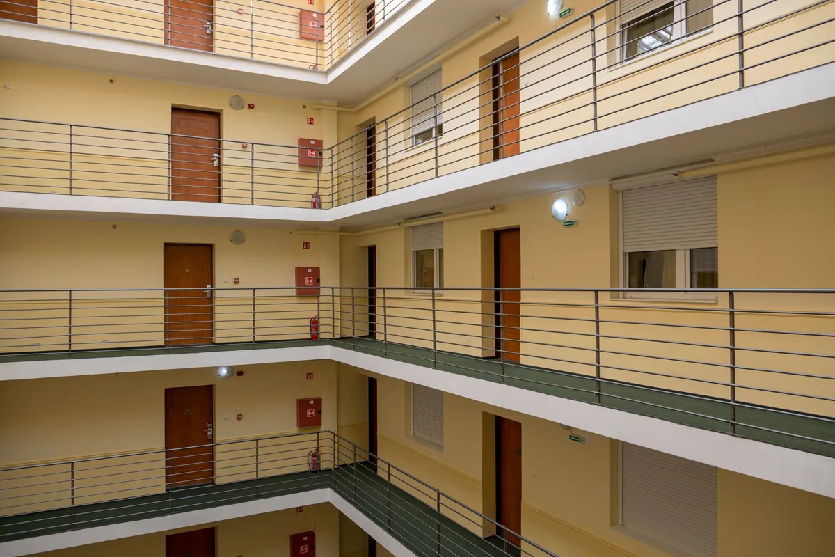The inner courtyard of an apartment block, with four walkway levels of wooden front doors, shuttered windows and steel railings stacked above one another.