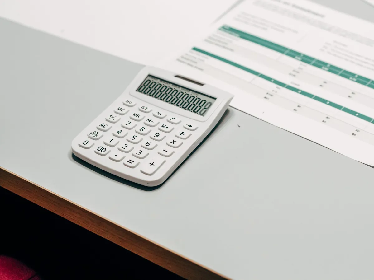 A white desktop calculator with all display segments lit, on a pale desk beside a printed sheet ruled into green and white table rows.