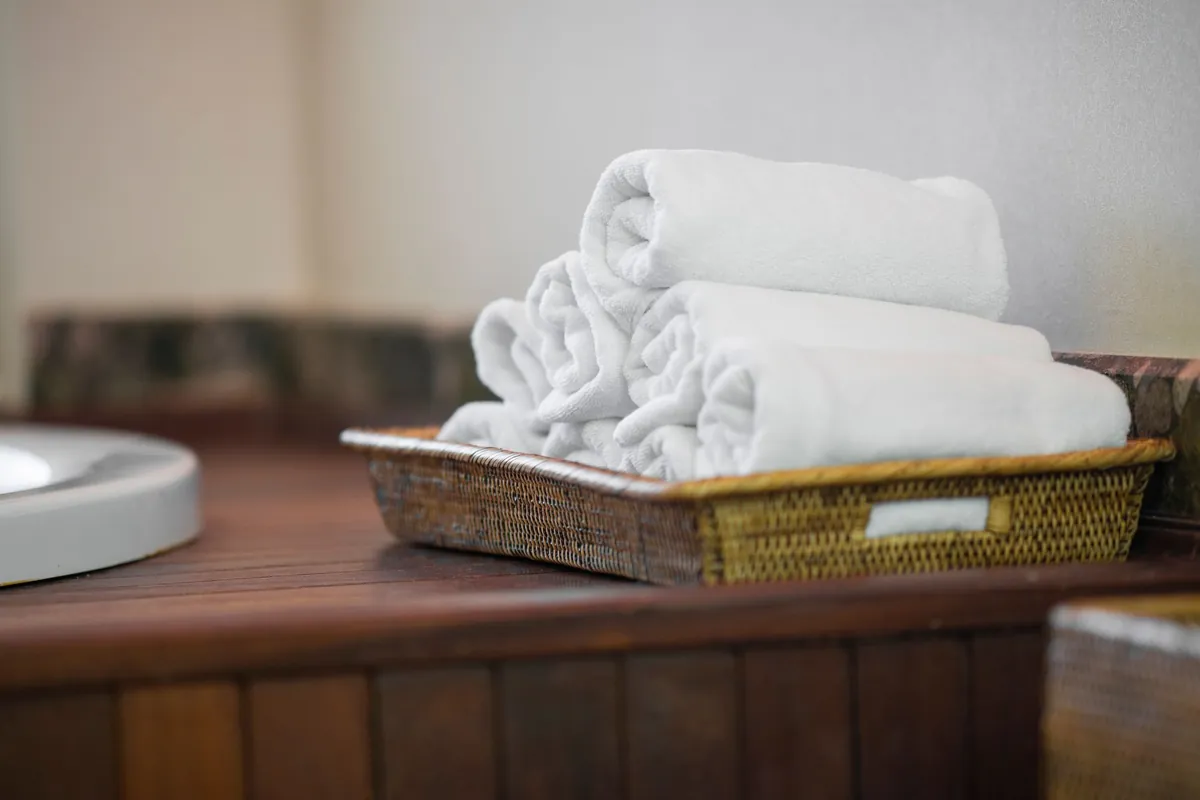 Rolled white towels in a wicker basket on a bathroom counter