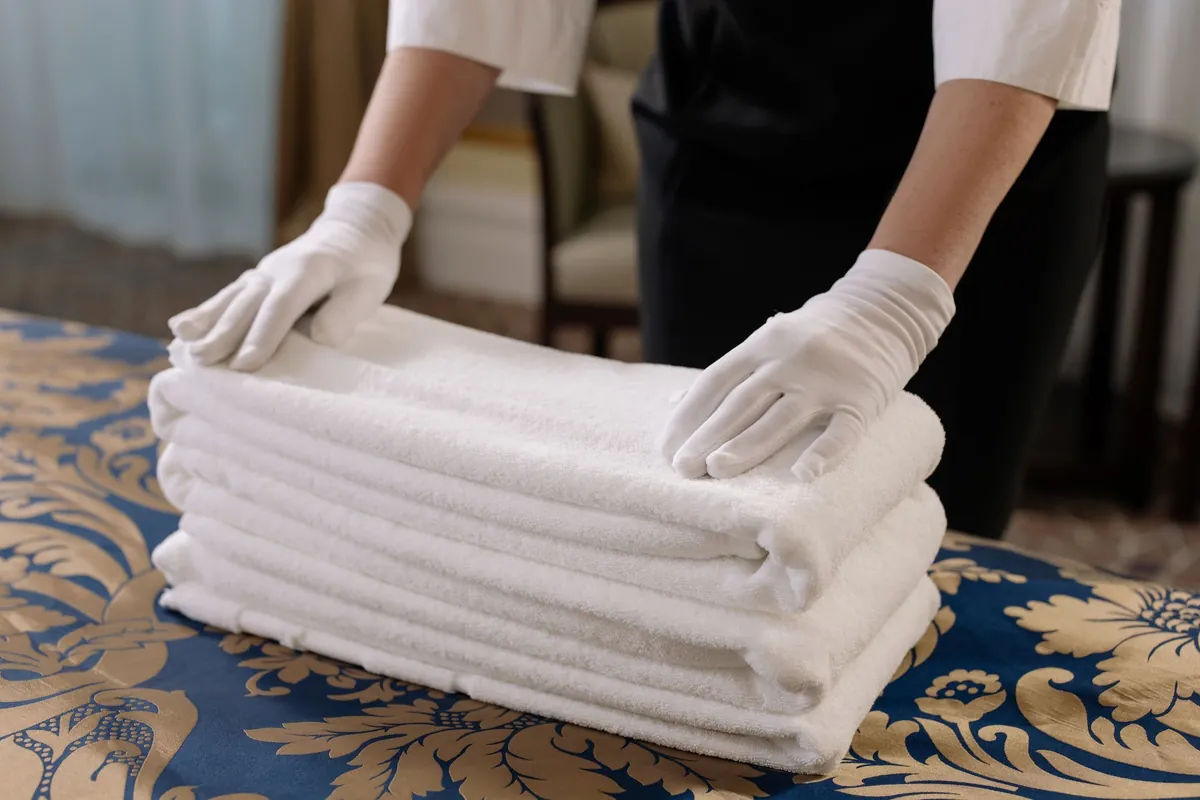 A housekeeper folding clean towels onto a made bed