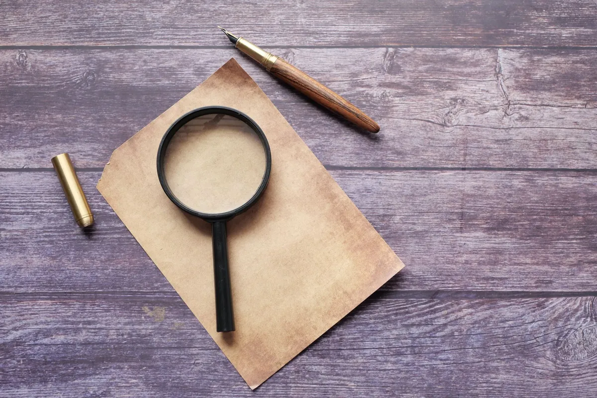 A magnifying glass and an old pen resting on a rustic wooden surface
