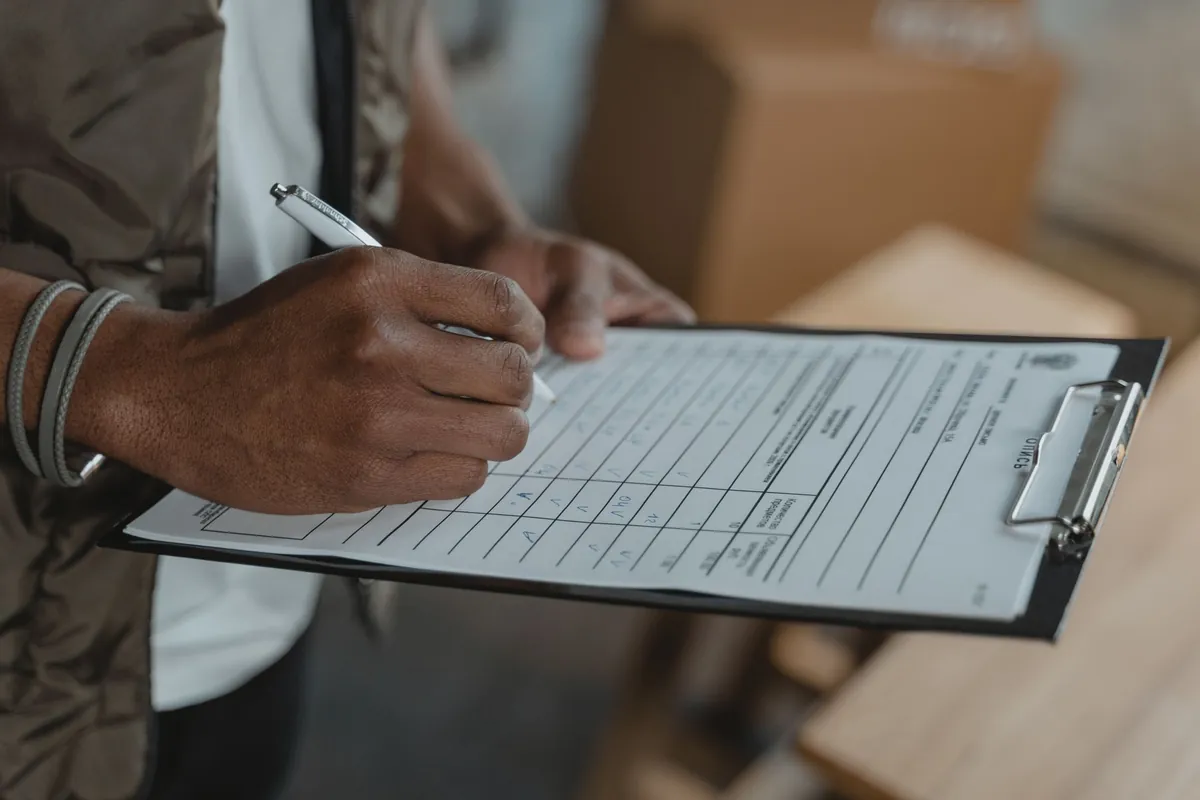 A hand completing a printed form on a clipboard