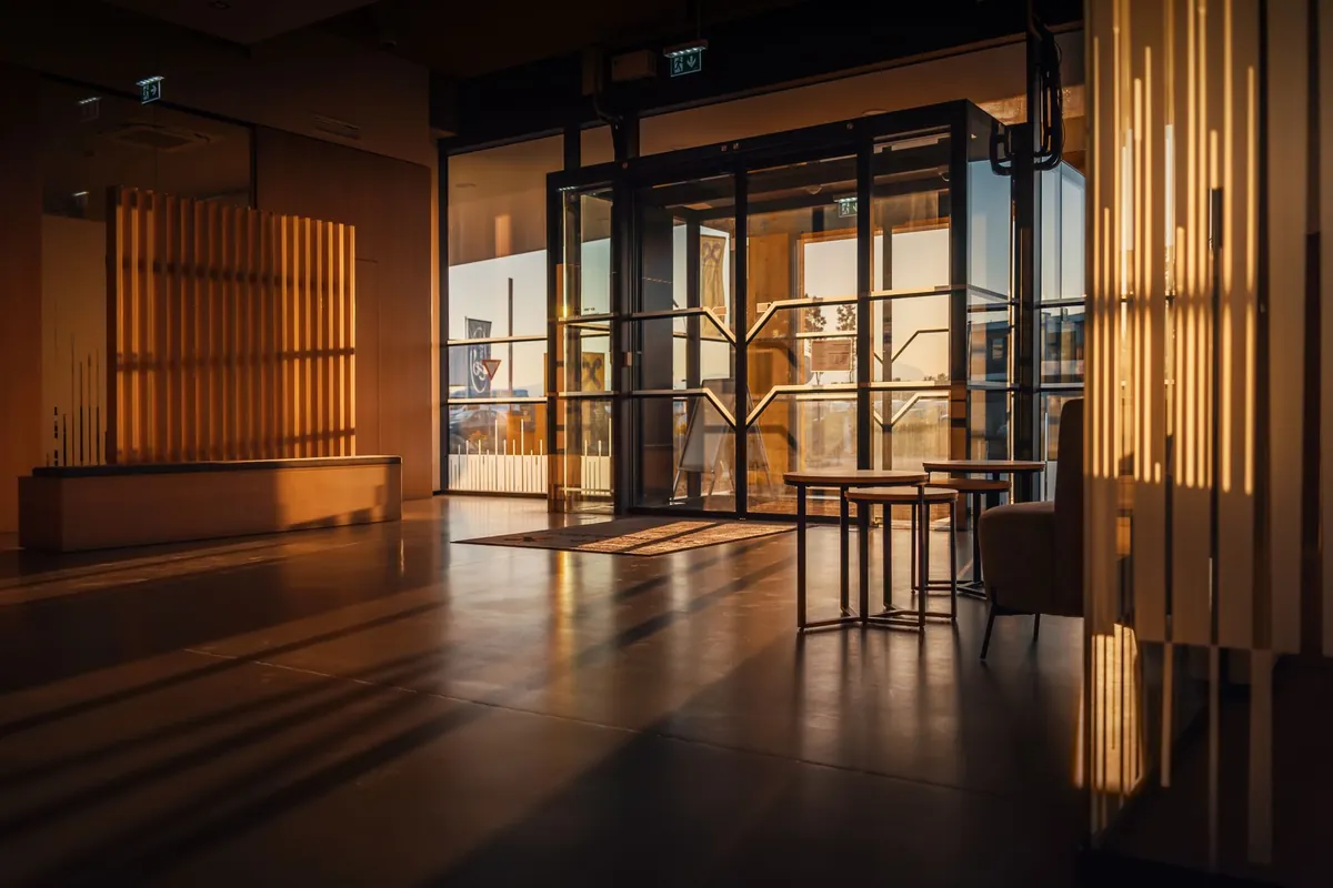 A modern hotel lobby with glass doors and warm wooden screens