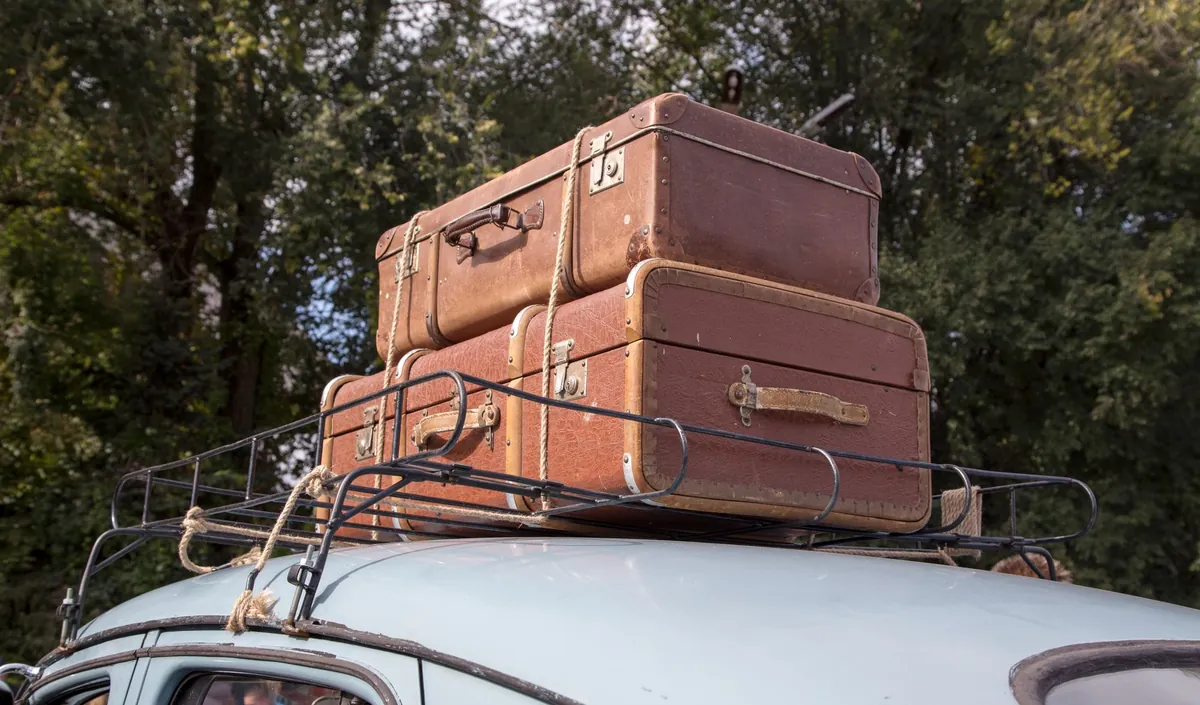 Two old leather suitcases strapped to the roof rack of a car