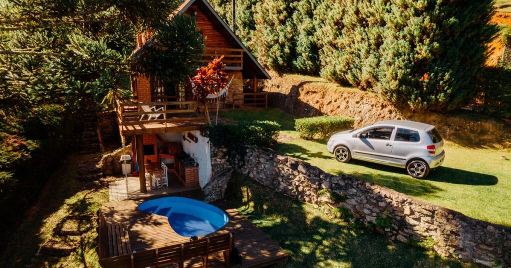 An aerial view of a wooden holiday house with a round pool and a car on the lawn