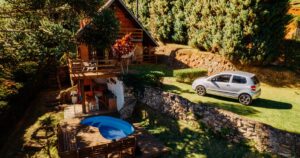 An aerial view of a wooden holiday house with a round pool and a car on the lawn