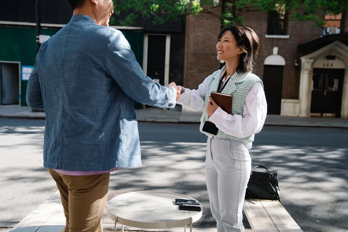 Two people shaking hands on a street outside a building