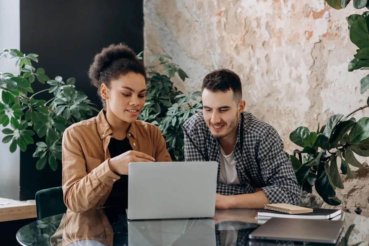 Two people sitting together at a laptop in a room with a brick wall