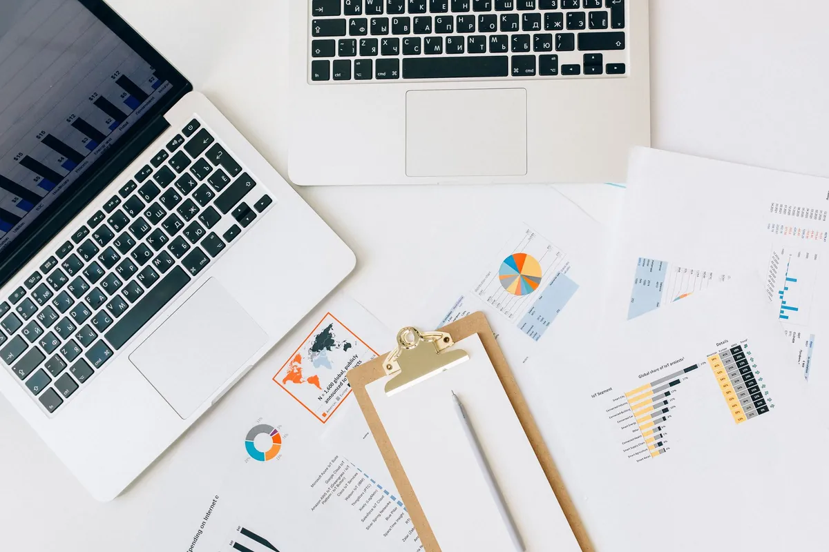 A flat lay of a laptop, a clipboard and printed charts on a white desk