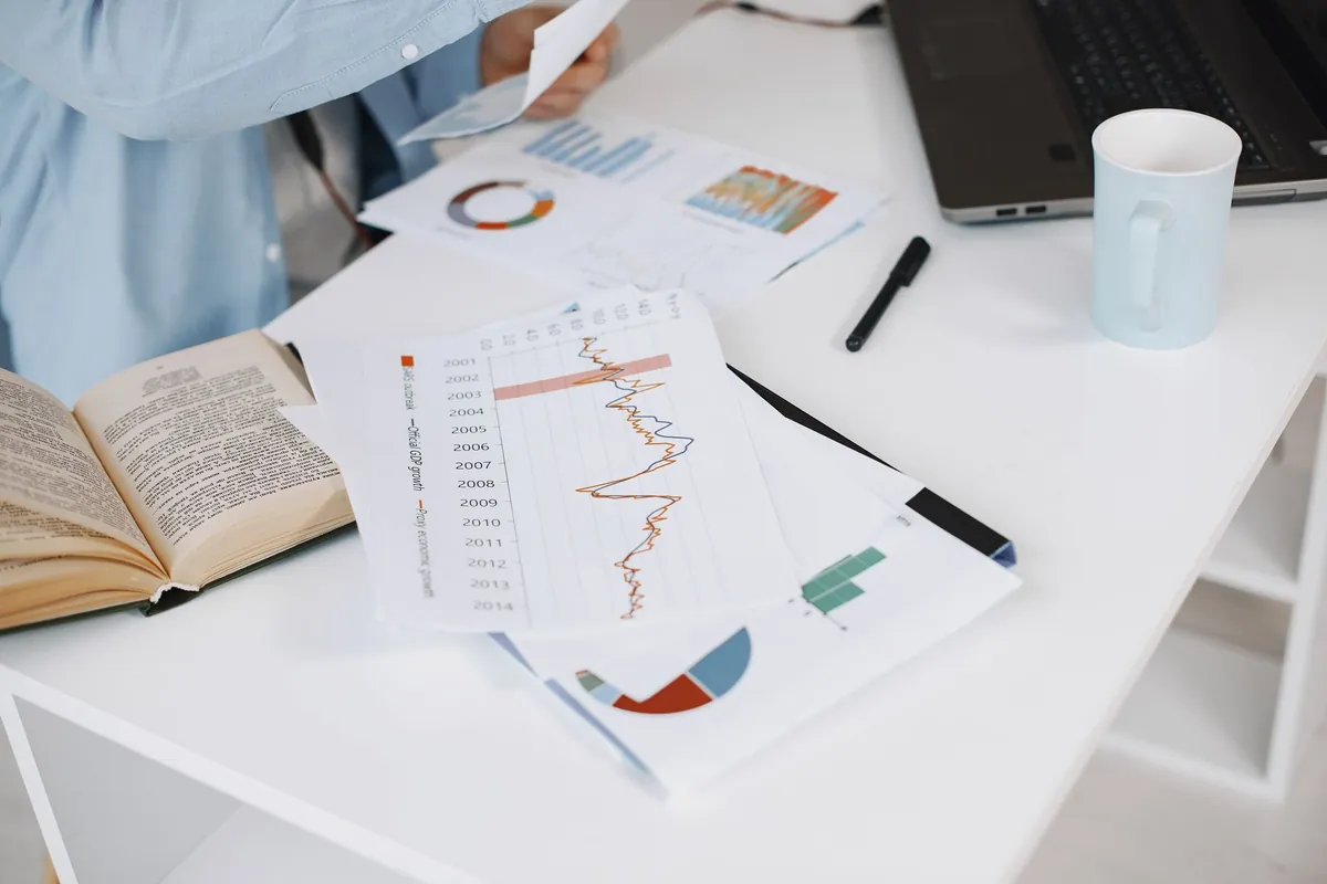 Printed rate charts and a notebook on a white desk, with a laptop to one side