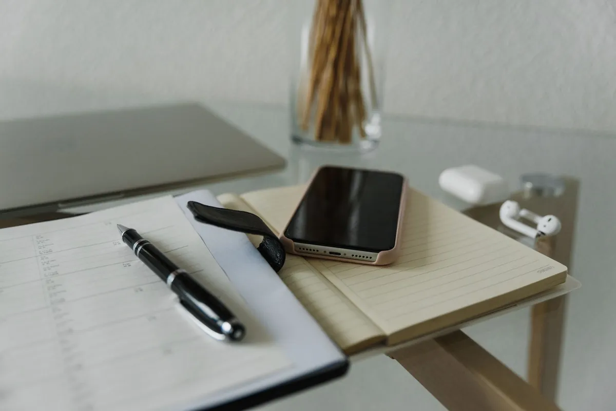 A quiet desk with a notebook, a pen and a phone face-down beside a closed laptop