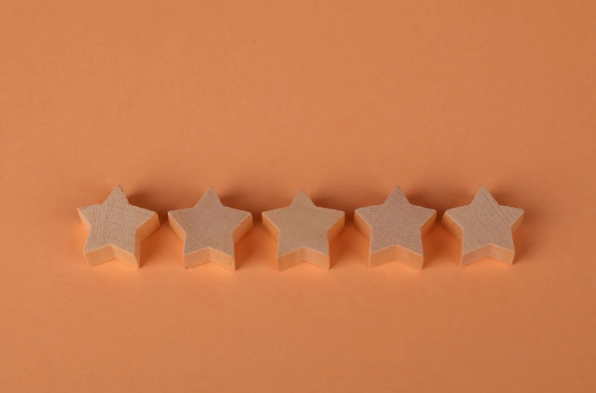 Five wooden star shapes in a row on a plain orange background