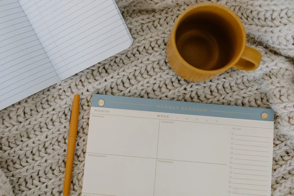 A blank weekly planner, a pen and a coffee mug on a knitted blanket