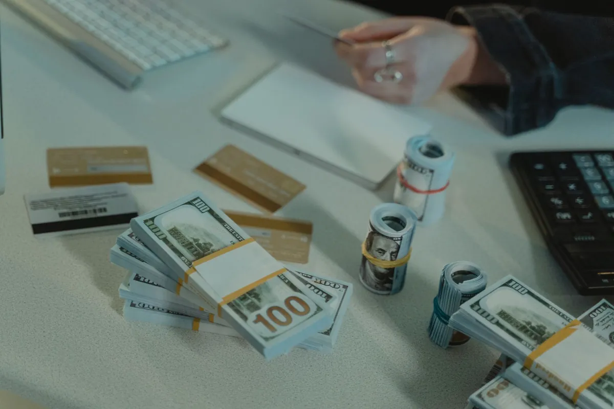 Cash, cards and a calculator on a desk with a hand holding a pen