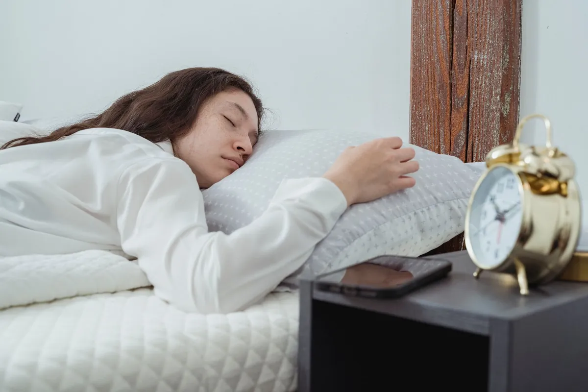A host asleep, phone face down on the bedside table beside a clock