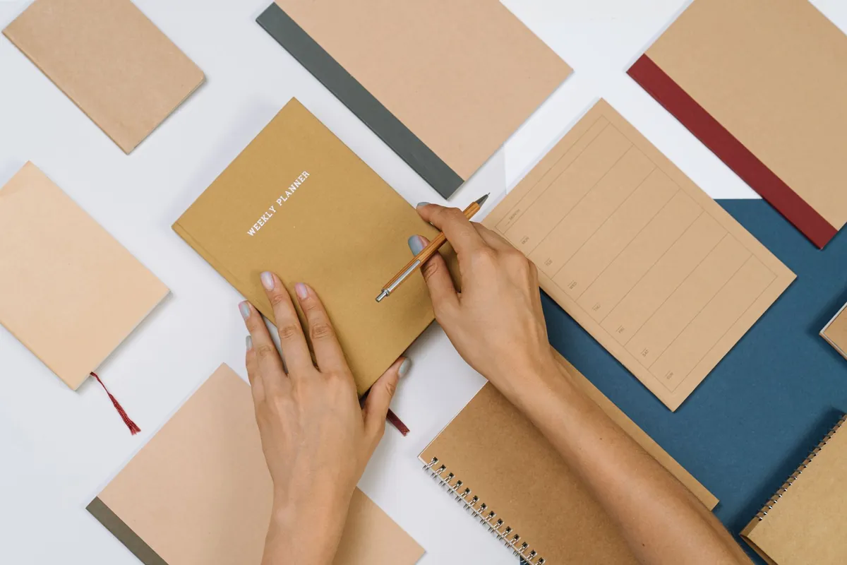 Hands writing in a plain notebook among tidy stationery on a desk