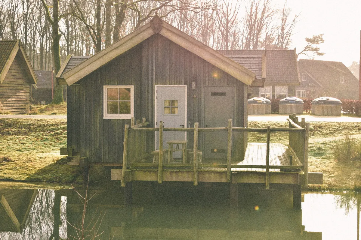 A wooden cabin beside its own dock on a quiet lake in sunshine