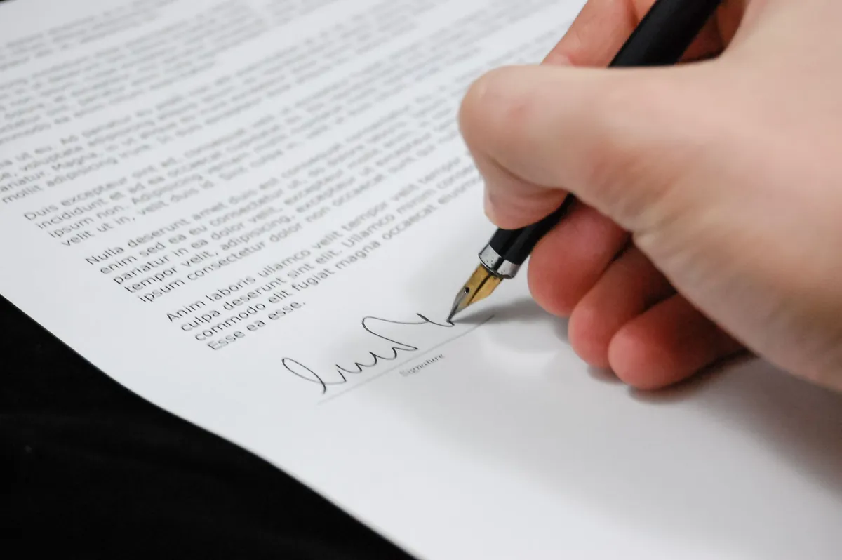 A hand signing the foot of a printed document with a fountain pen
