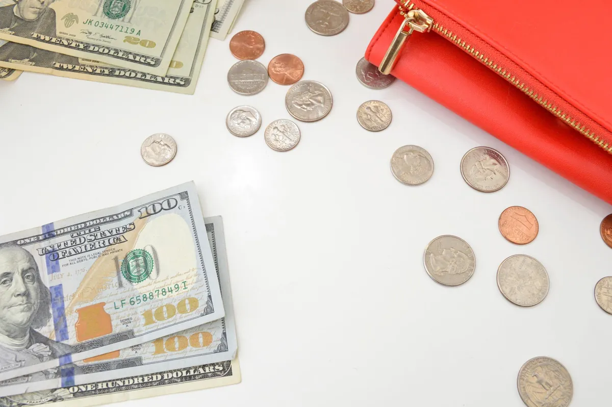 Dollar notes and loose coins scattered beside a red purse