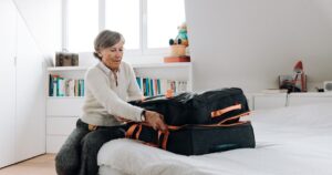 A woman packing a black suitcase on a bed in a bright attic bedroom