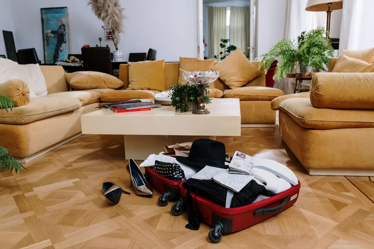 An open red suitcase with clothes spilling out on a living-room floor, shoes beside it