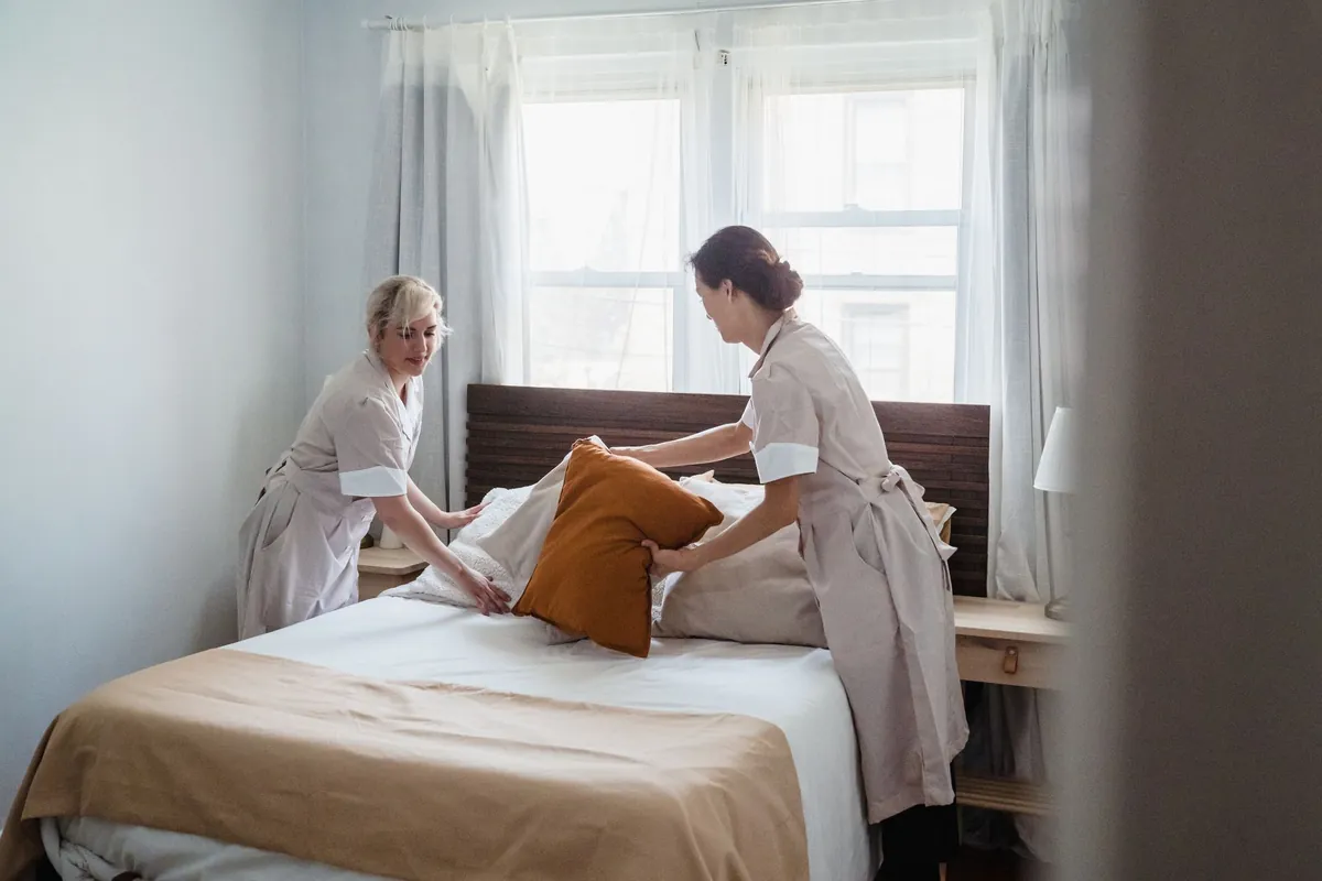 Two housekeepers arranging pillows on a bed in a bright bedroom