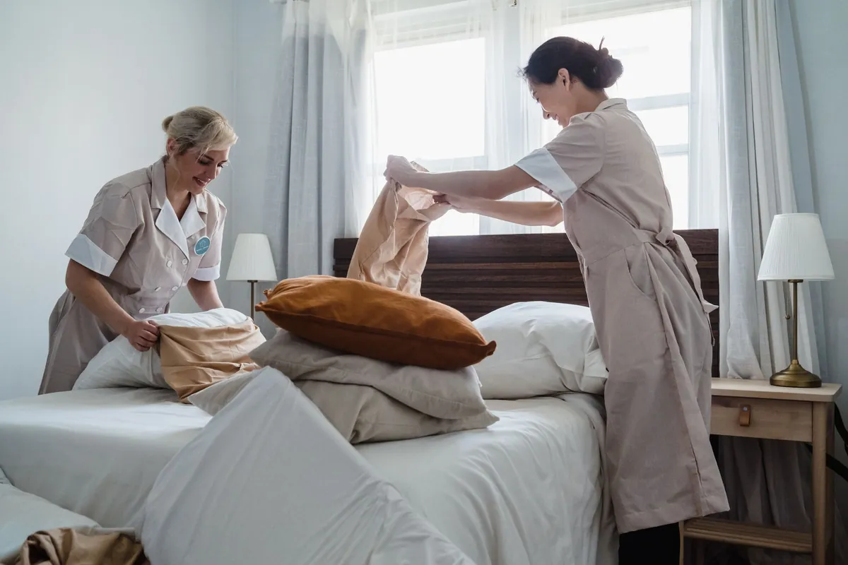 Two housekeepers changing bed linens in a guest room.