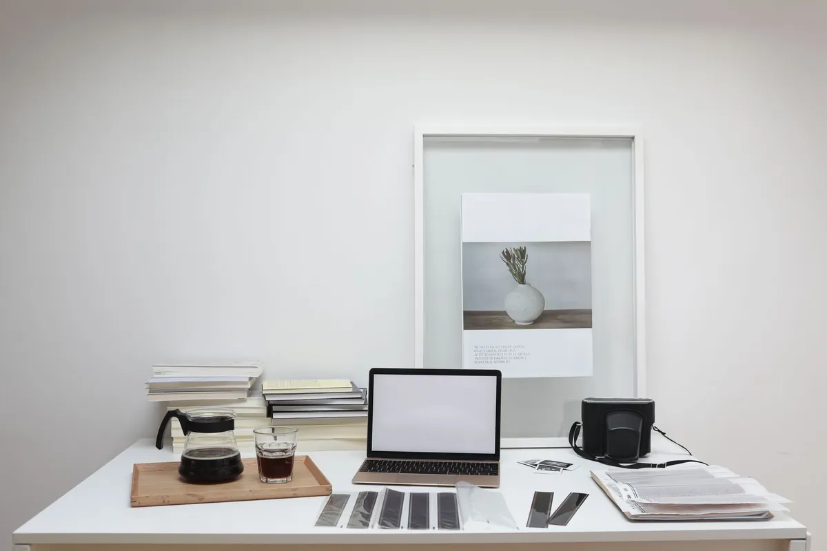 Desk with stacks of books, printed sheets, paper samples, and an open laptop.