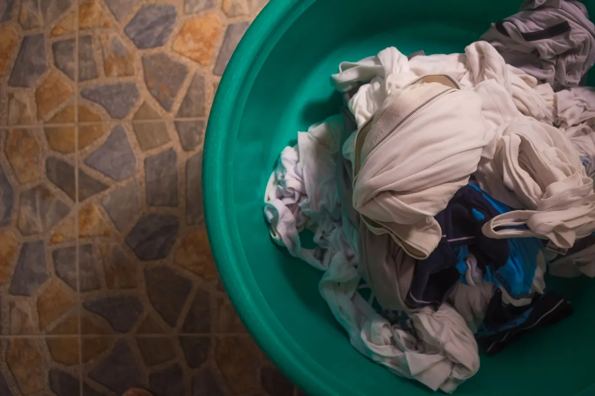 Overhead view of a laundry basket filled with folded clothes on a tiled floor.