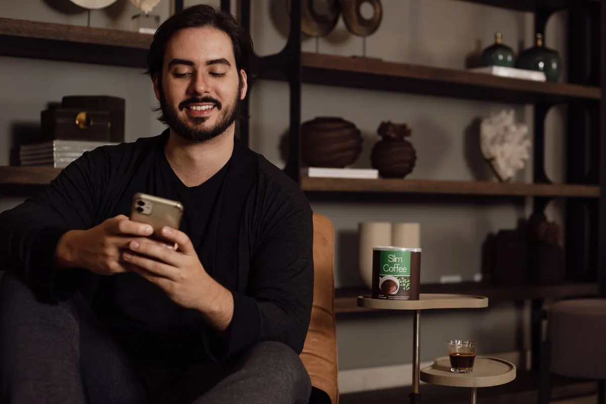 Smiling bearded man using a smartphone while sitting on a sofa in a cozy living room