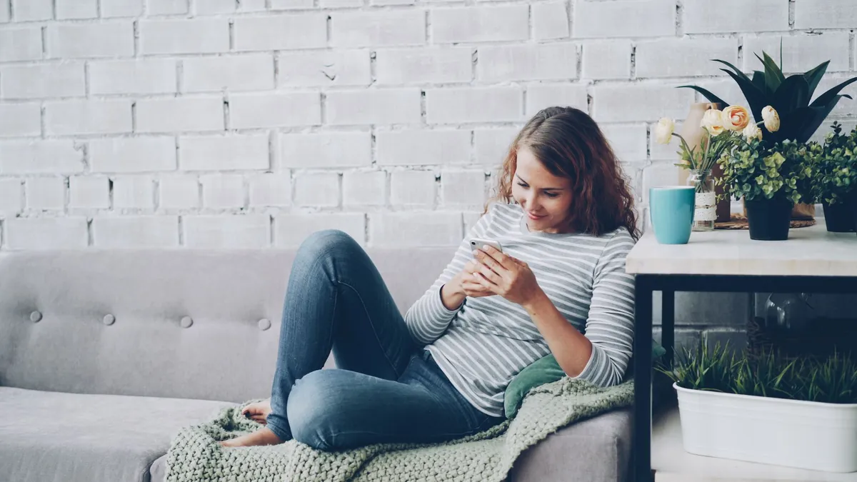 Woman relaxing on a couch while using her smartphone in a cozy living room with plants.