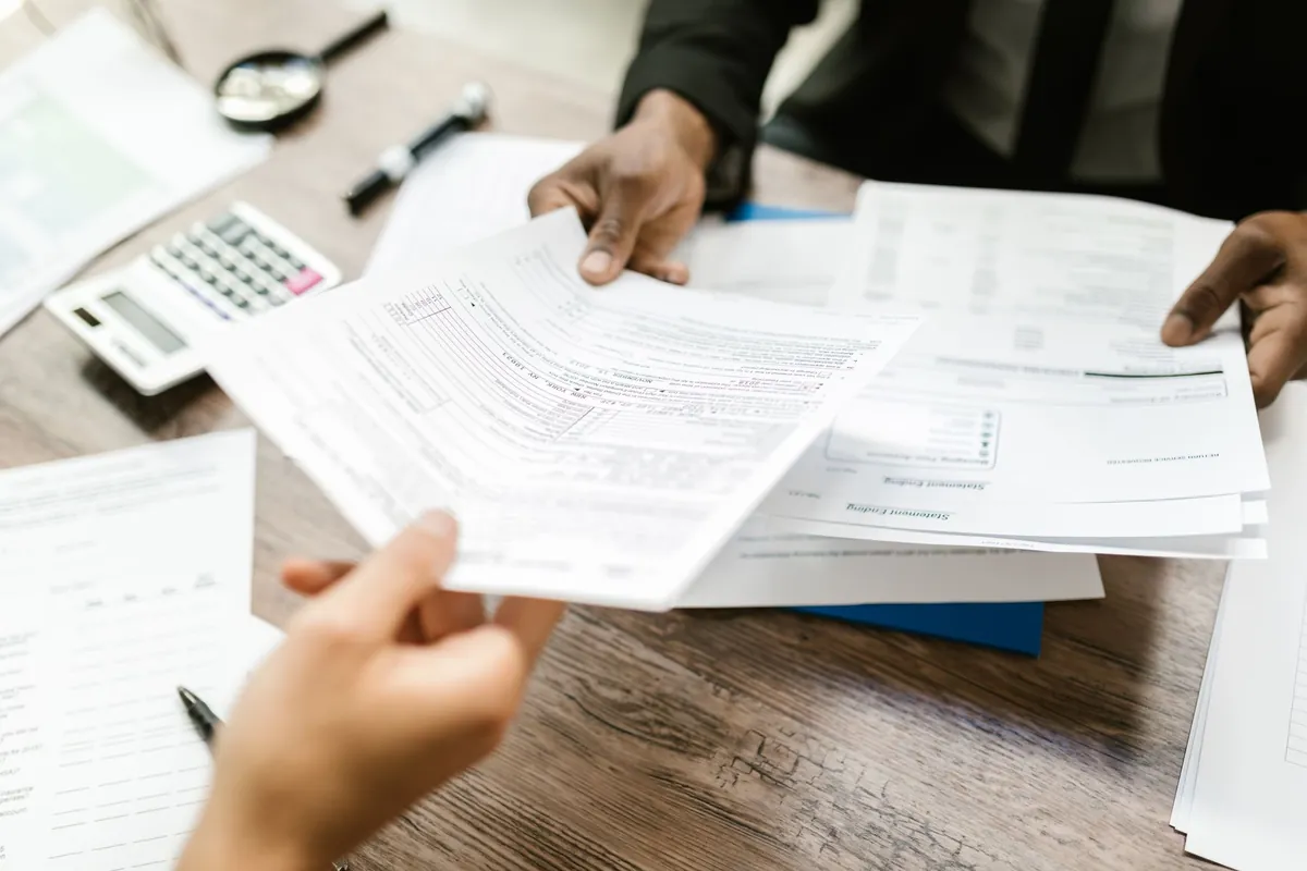 Two professionals exchanging documents across a desk in an office