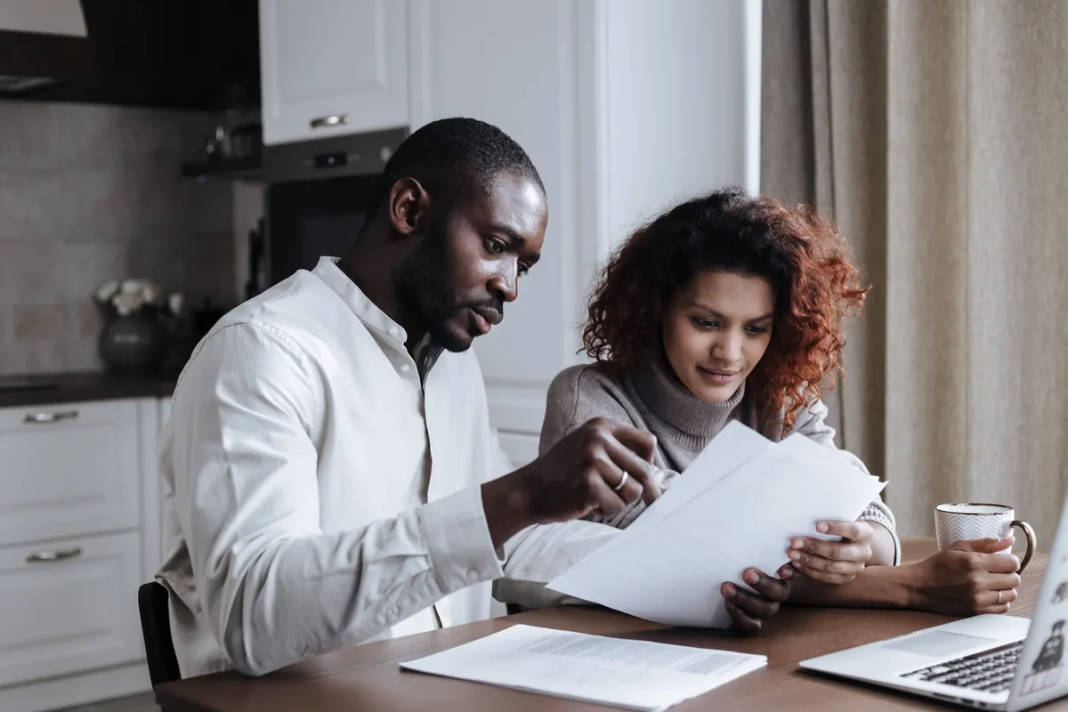 Couple sitting together at home reviewing paperwork and using a laptop
